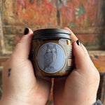 Someone holding the White Lodge Soy Wax 3 oz Candle in front of a wooden background.