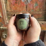 Someone holding the Green Fairy Soy Wax 3 oz Candle in front of a wooden background.