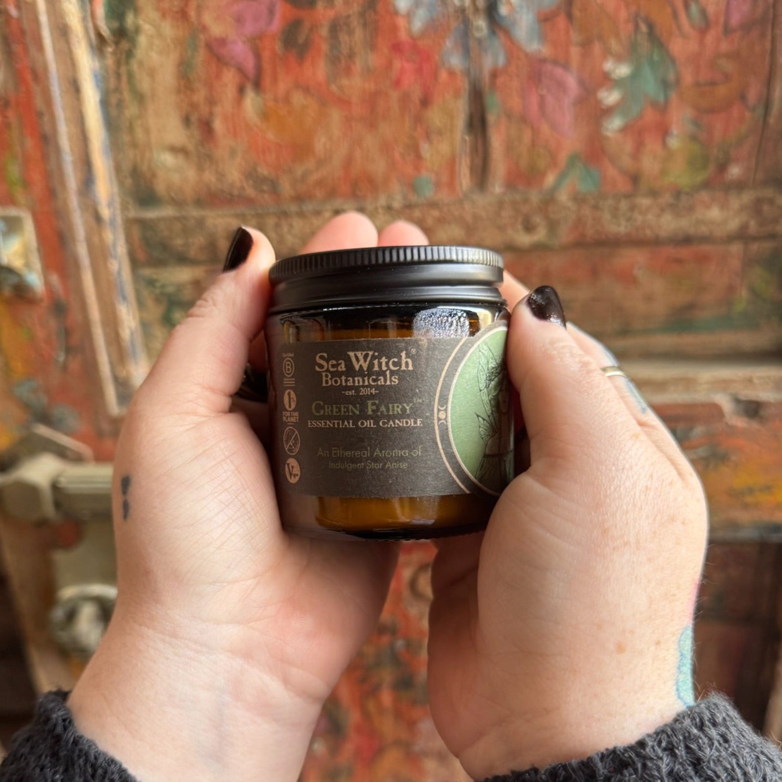 Someone holding the Green Fairy Soy Wax 3 oz Candle in front of a wooden background.
