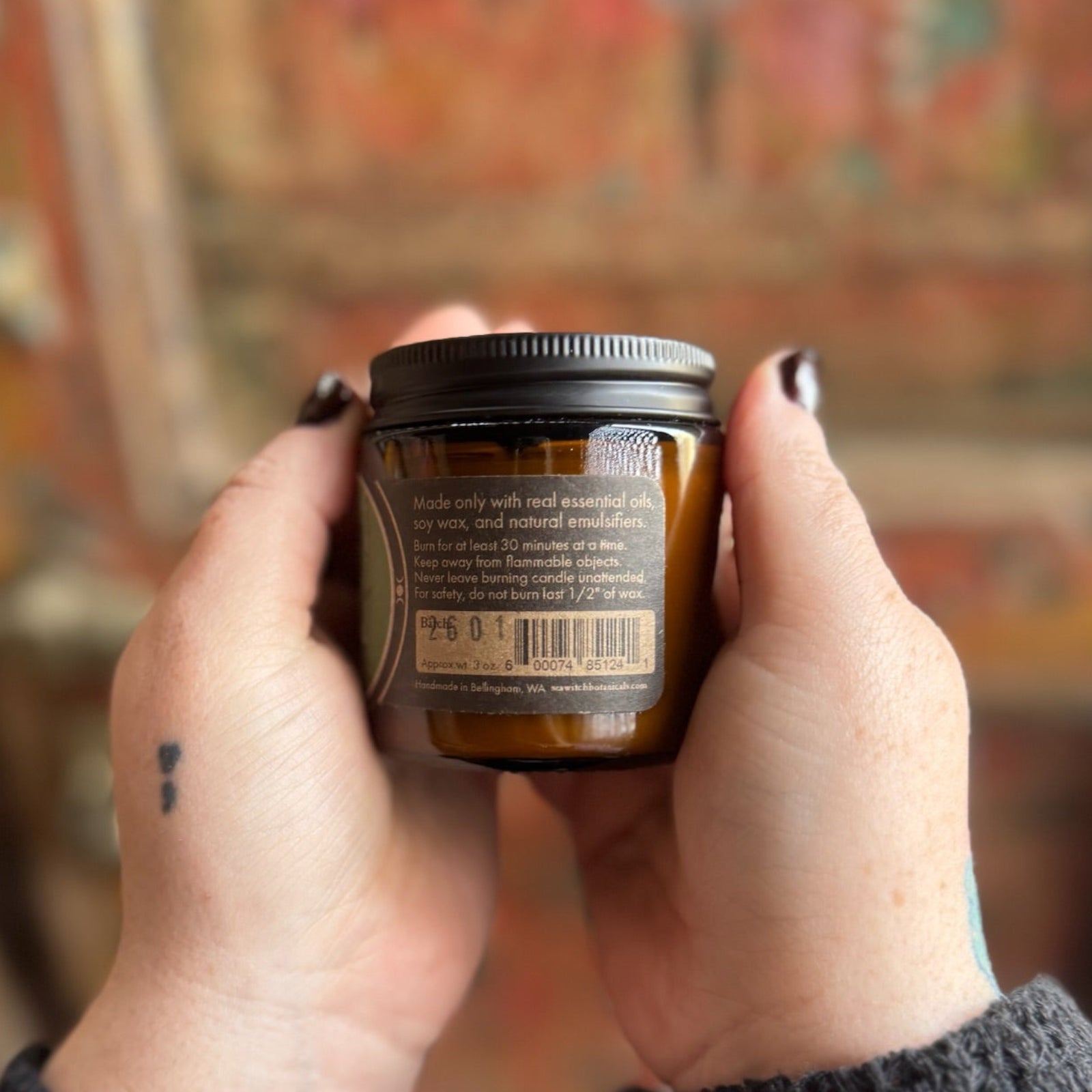 Someone holding the Green Fairy Soy Wax 3 oz Candle in front of a wooden background.
