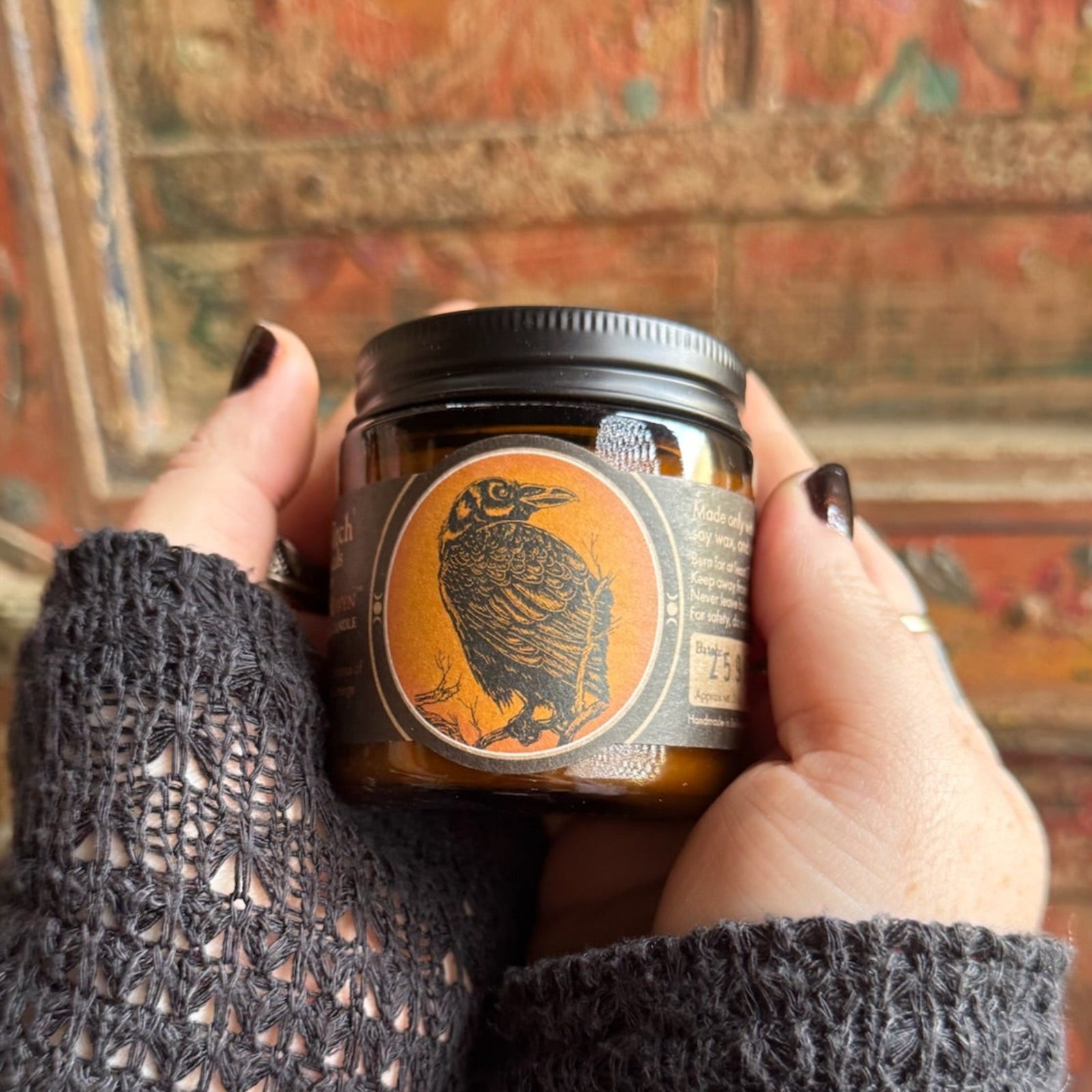 Someone holding the Quoth the Raven Soy Wax 3 oz Candle in front of a wooden background.
