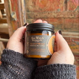 Someone holding the Quoth the Raven Soy Wax 3 oz Candle in front of a wooden background.