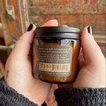 Someone holding the Quoth the Raven Soy Wax 3 oz Candle in front of a wooden background.