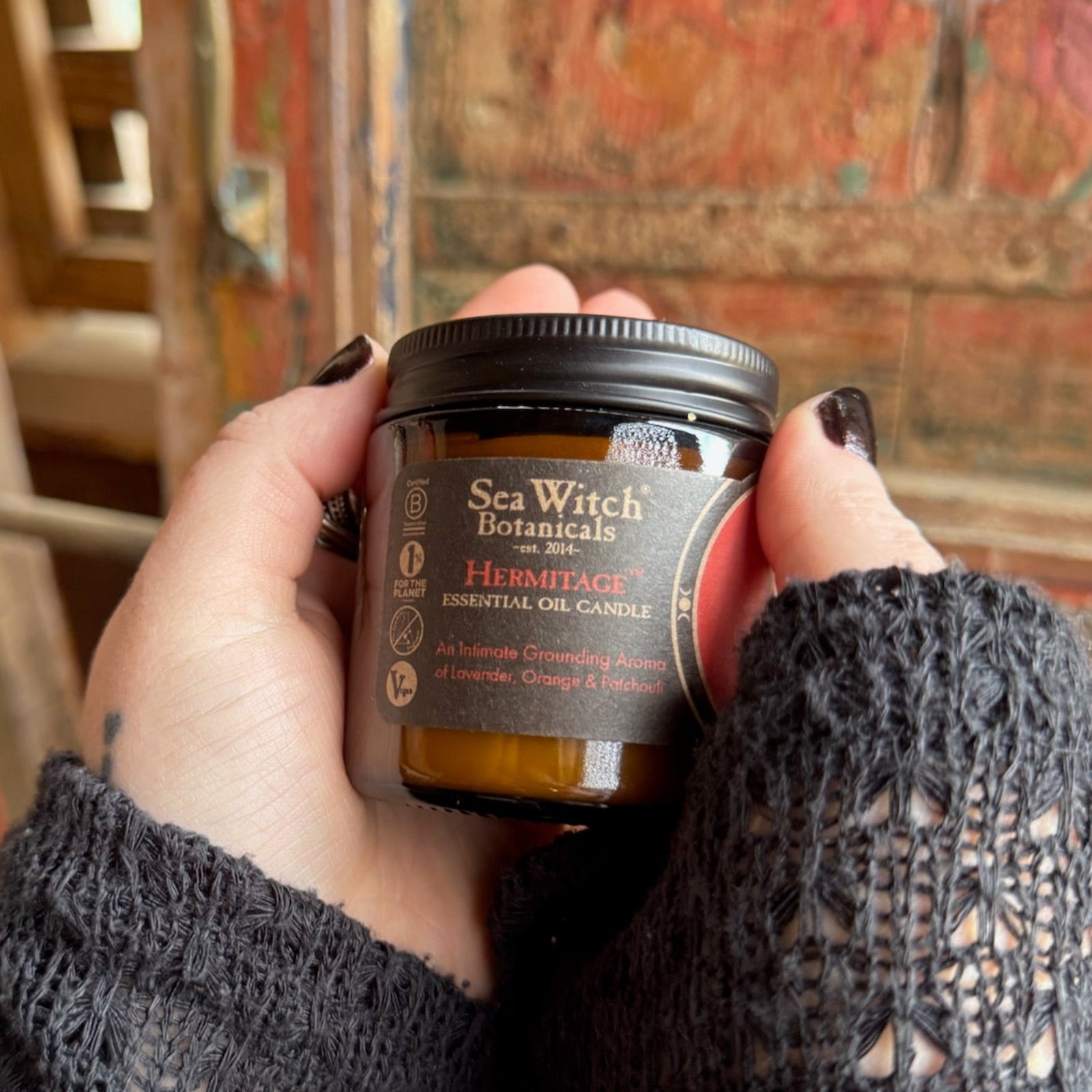 Someone holding the Hermitage Soy Wax 3 oz Candle in front of a wooden background.
