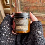 Someone holding the Hermitage Soy Wax 3 oz Candle in front of a wooden background.