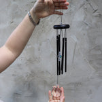 Someone holding the Black Crystal Meditation Woodstock Wind Chime in front of a white wall.