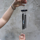 Someone holding the Black Crystal Meditation Woodstock Wind Chime in front of a white wall.