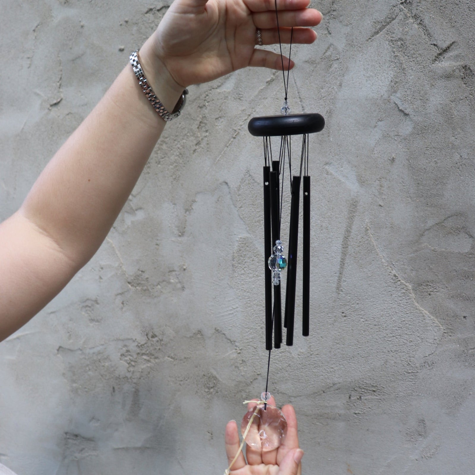 Someone holding the Black Crystal Meditation Woodstock Wind Chime in front of a white wall.