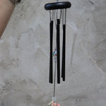 Someone holding the Black Crystal Meditation Woodstock Wind Chime in front of a white wall.