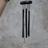 Someone holding the Black Crystal Meditation Woodstock Wind Chime in front of a white wall.