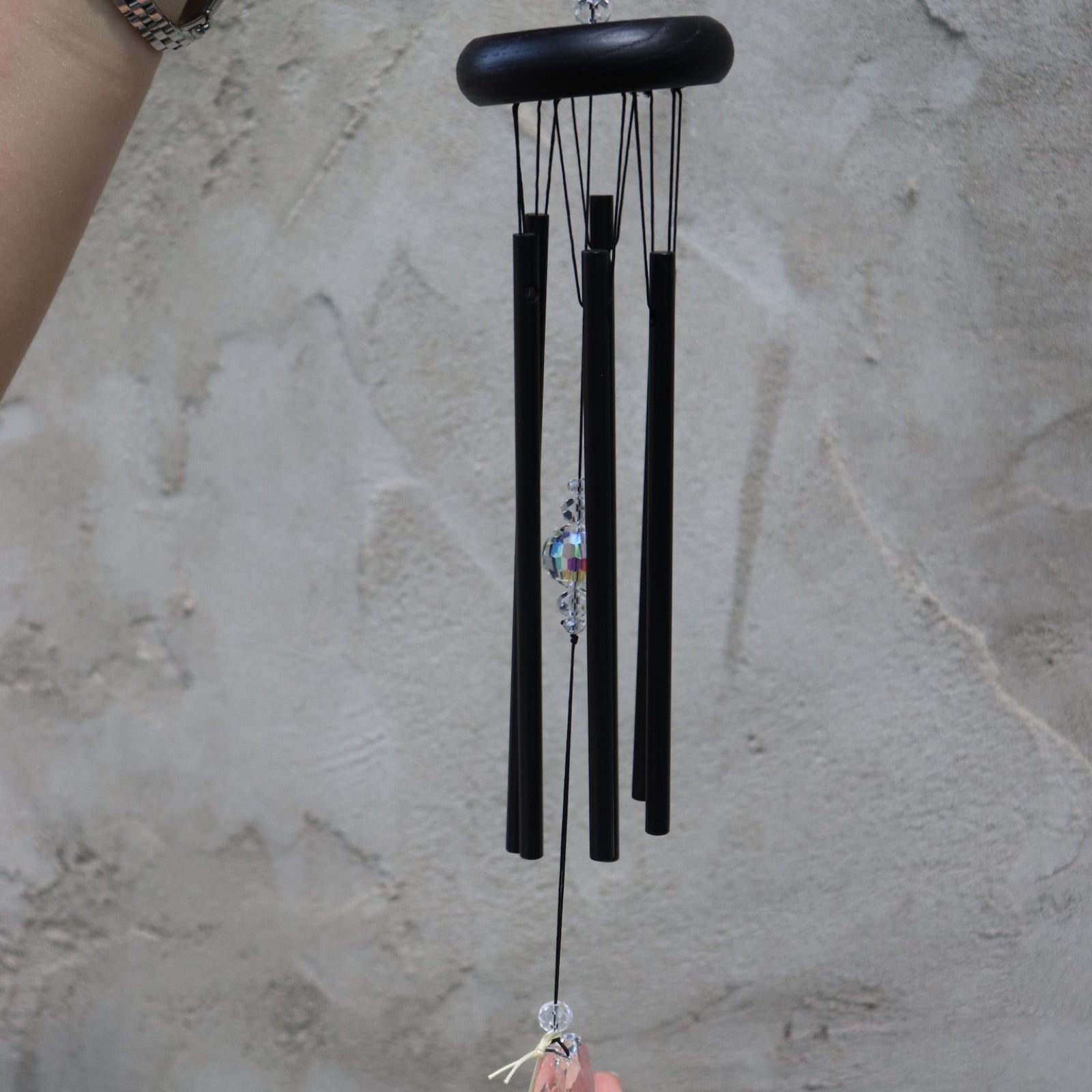 Someone holding the Black Crystal Meditation Woodstock Wind Chime in front of a white wall.