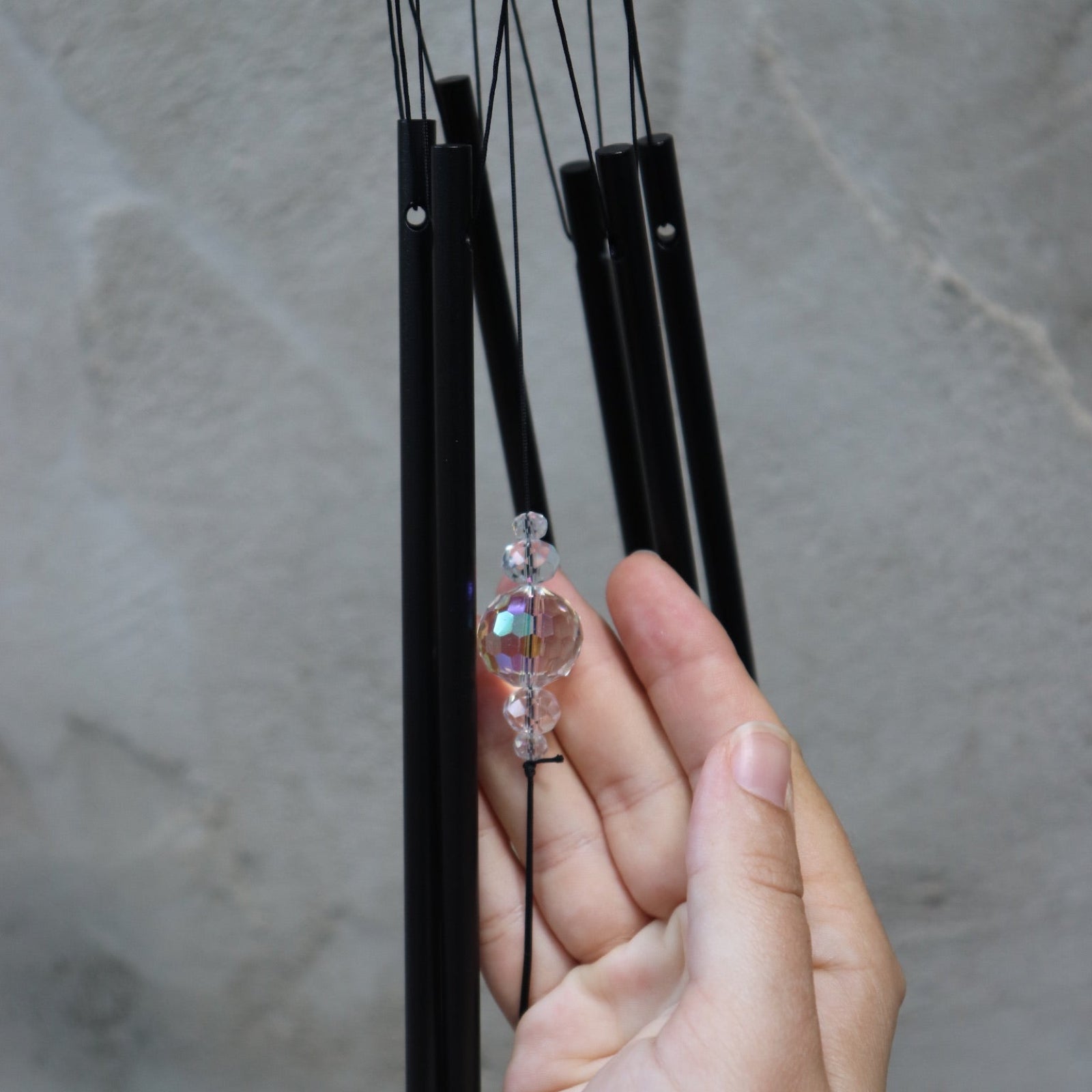 An up-close image of someone holding the Black Crystal Meditation Woodstock Wind Chime in front of a white wall.