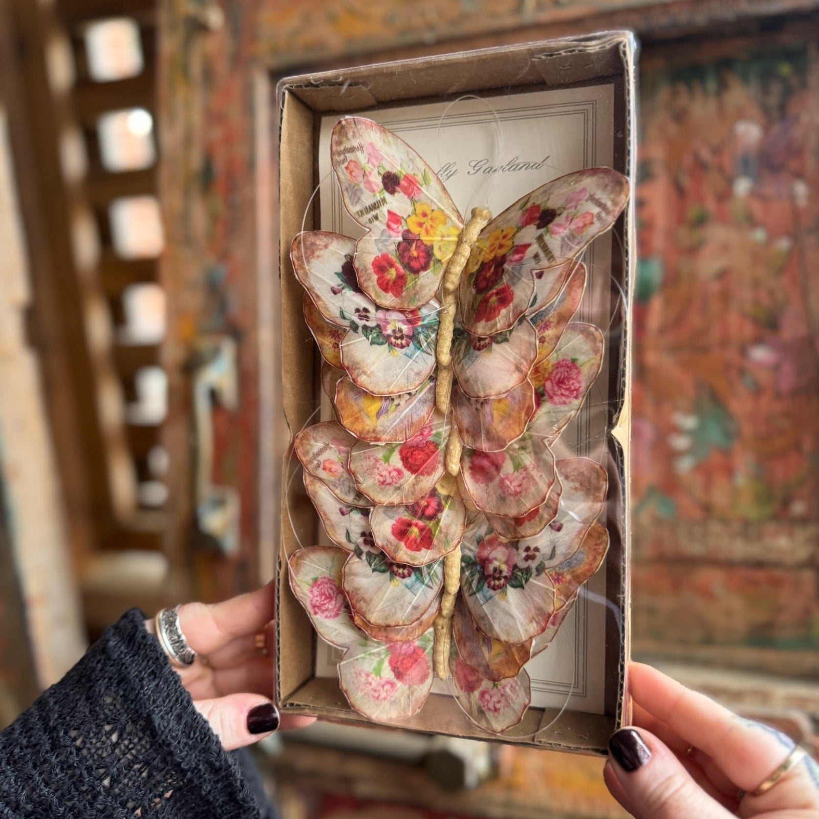 Someone holding the Seville Butterfly Garland - Vintage Floral Butterfly Garland in front of a wooden background.