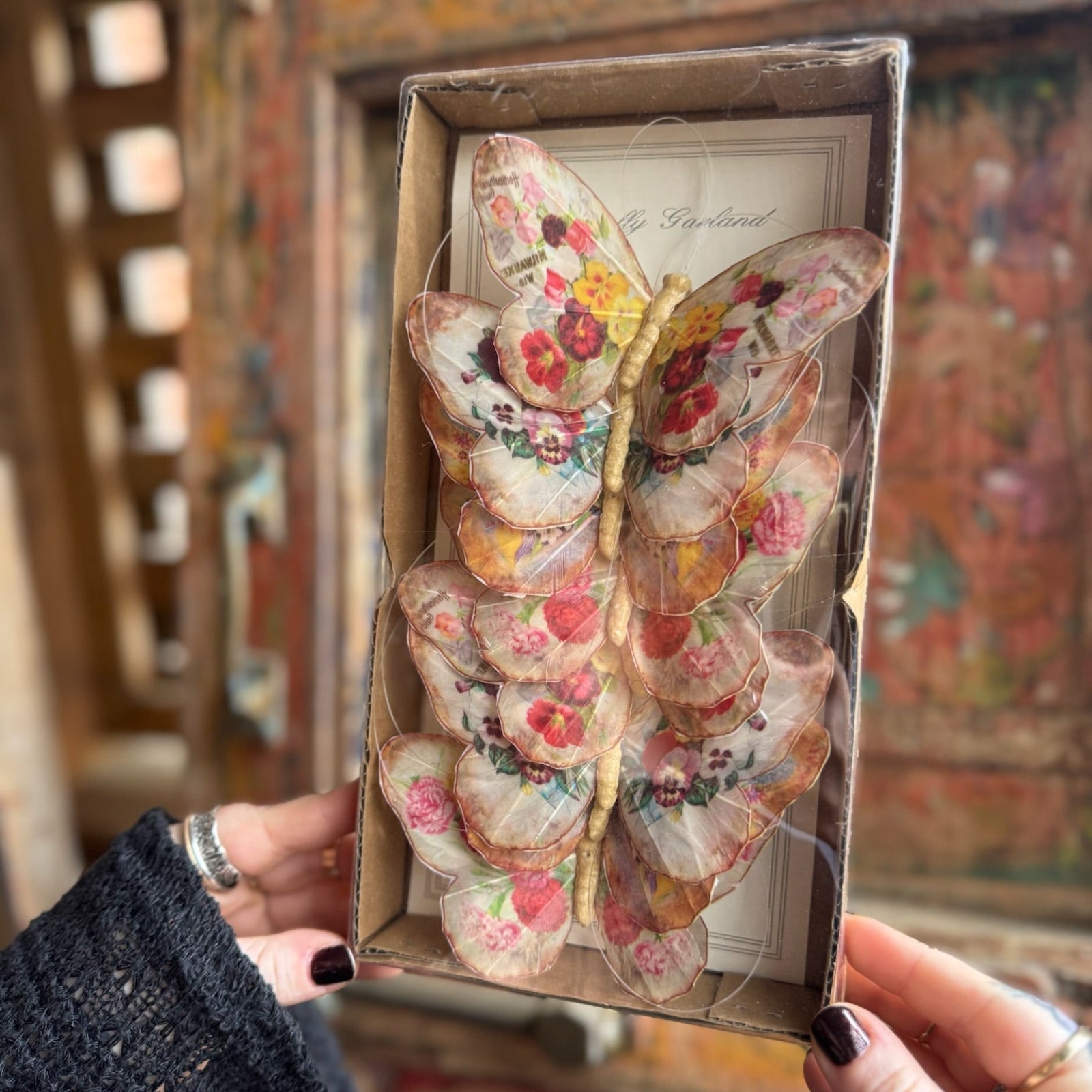 Someone holding the Seville Butterfly Garland - Vintage Floral Butterfly Garland in front of a wooden background.