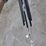An up-close image of someone holding the Black Crystal Meditation Woodstock Wind Chime in front of a white wall.