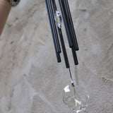 An up-close image of someone holding the Black Crystal Meditation Woodstock Wind Chime in front of a white wall.