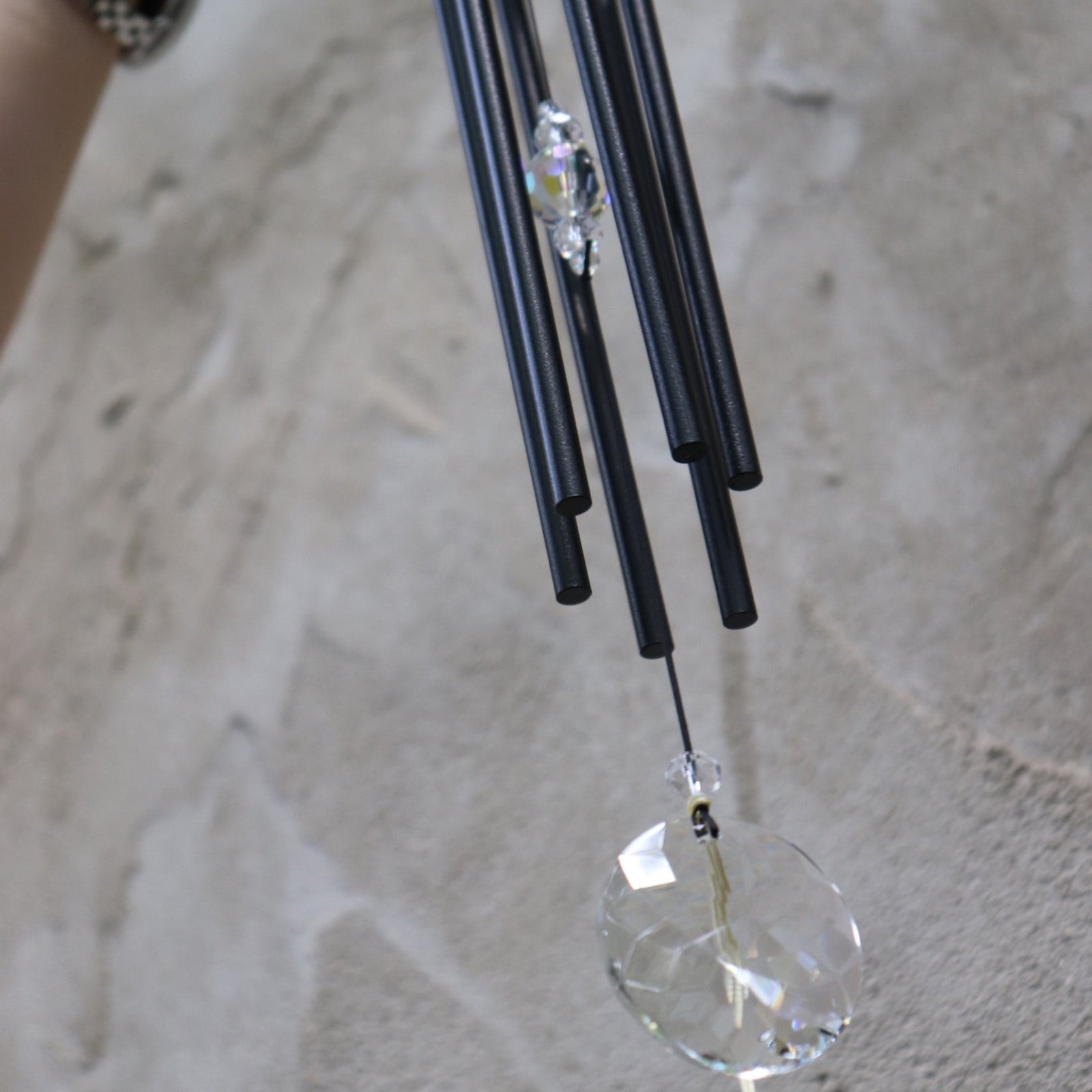 An up-close image of someone holding the Black Crystal Meditation Woodstock Wind Chime in front of a white wall.