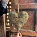 Someone holding the Ashia Gold Metal Heart Tea Light Holder in front of a wooden background.