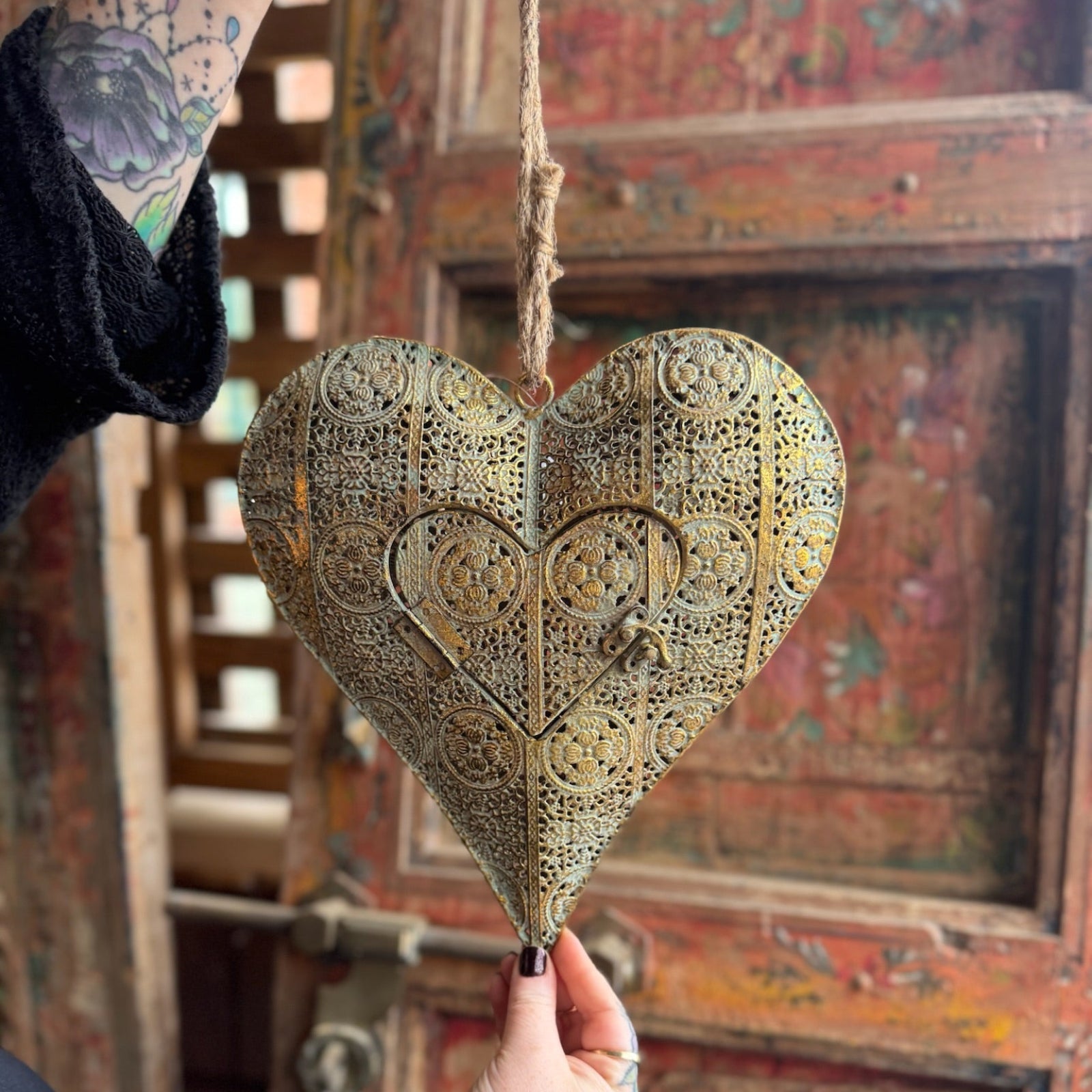 Someone holding the Ashia Gold Metal Heart Tea Light Holder in front of a wooden background.