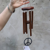 Someone holding the Peace Woodstock Wind Chime in front of a white wall.