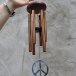 Someone holding the Peace Woodstock Wind Chime in front of a white wall.