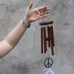 Someone holding the Peace Woodstock Wind Chime in front of a white wall.