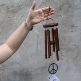Someone holding the Peace Woodstock Wind Chime in front of a white wall.
