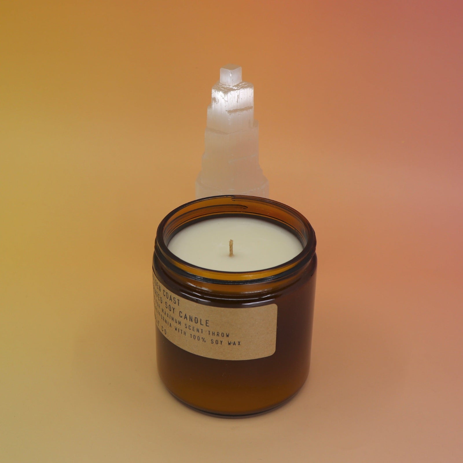 The Golden Coast - 12.5 oz Large Concentrated Soy Wax Candle in front of a selenite tower all on a pink and yellow background.