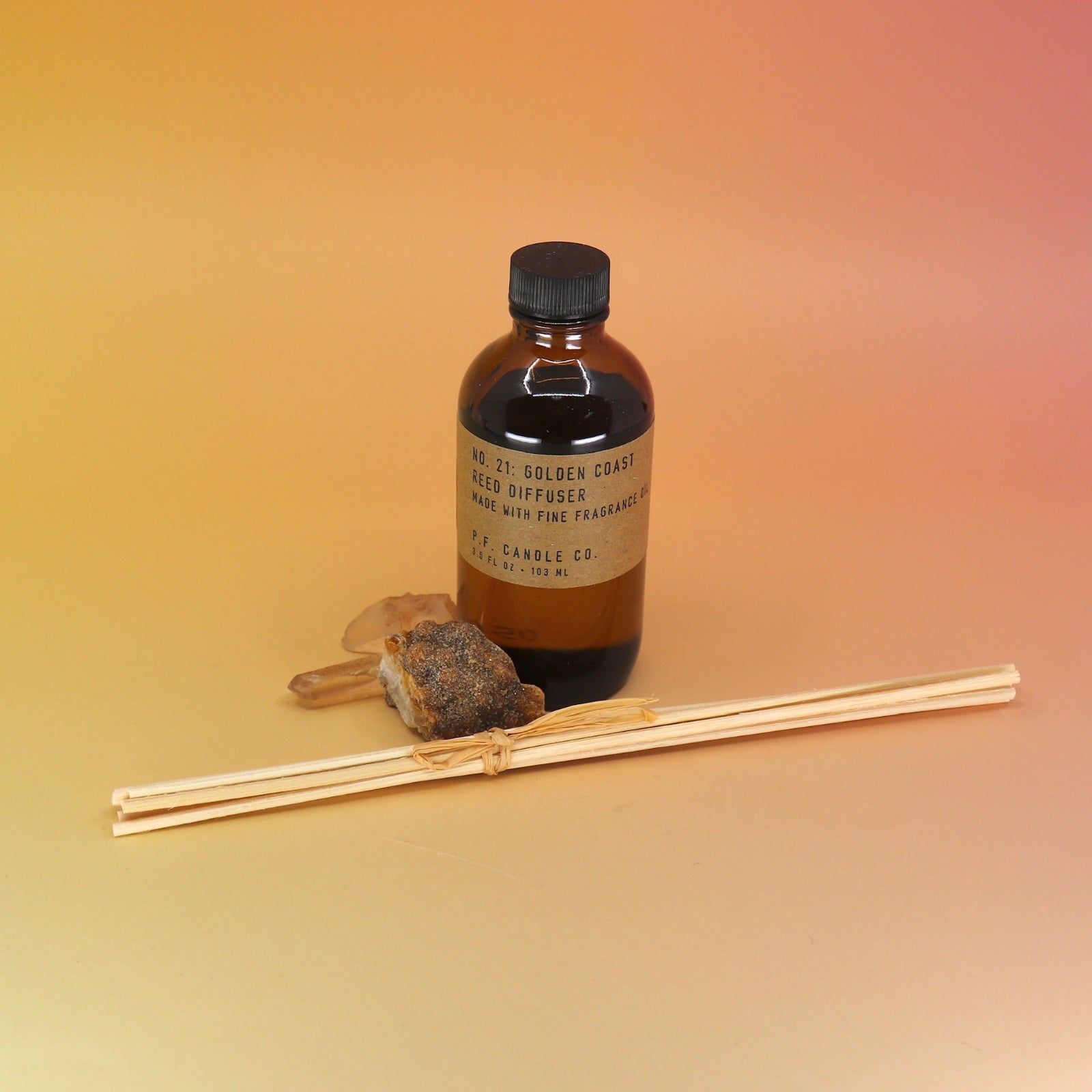 The P.F. Candle Co. Golden Coast - 3.5 oz Reed Diffuser on a pink and yellow background.