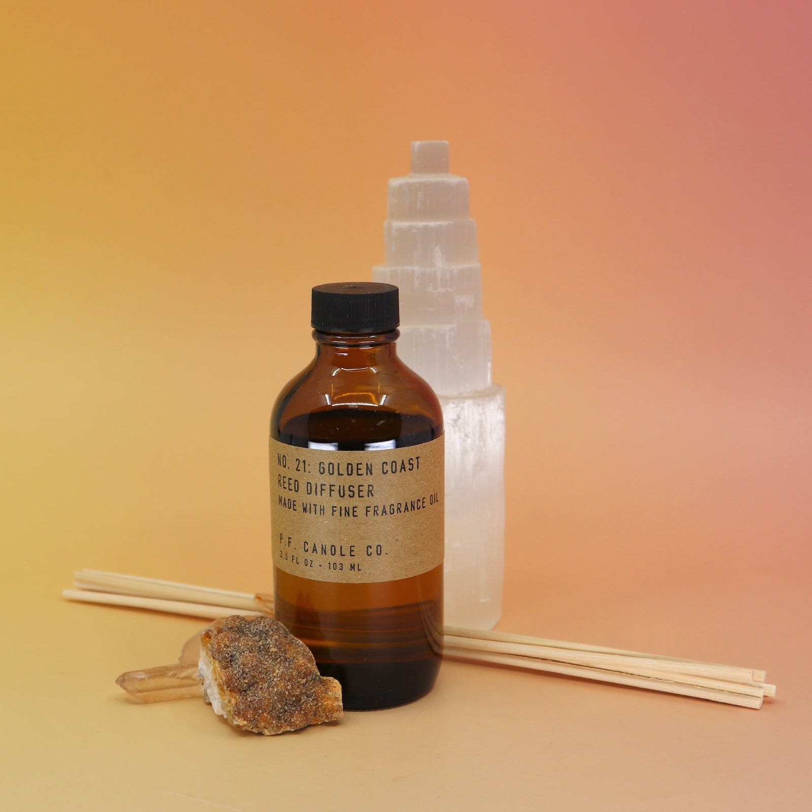 The P.F. Candle Co. Golden Coast - 3.5 oz Reed Diffuser in front of a selenite tower on a pink and yellow background.
