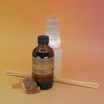 The back of the P.F. Candle Co. Golden Coast - 3.5 oz Reed Diffuser in front of a selenite tower on a pink and yellow background.