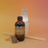 The back of the P.F. Candle Co. Golden Coast - 3.5 oz Reed Diffuser in front of a selenite tower on a pink and yellow background.