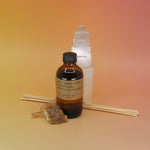 The Amber & Moss - 3.5 oz Reed Diffuser - P.F. Candle Co. in front of a selenite tower all on a pink and yellow background.