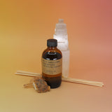 The Amber & Moss - 3.5 oz Reed Diffuser - P.F. Candle Co. in front of a selenite tower all on a pink and yellow background.