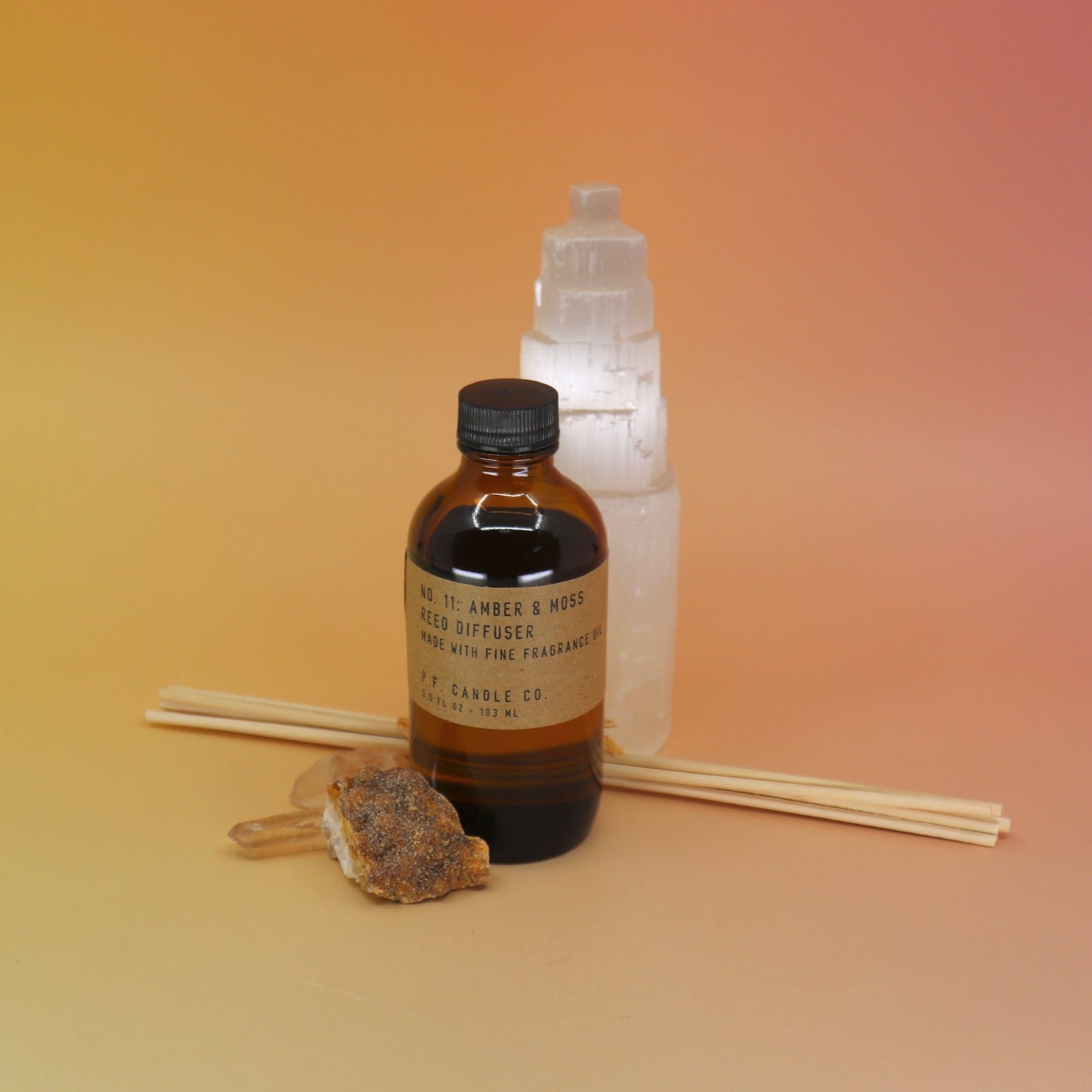 The Amber & Moss - 3.5 oz Reed Diffuser - P.F. Candle Co. in front of a selenite tower all on a pink and yellow background.