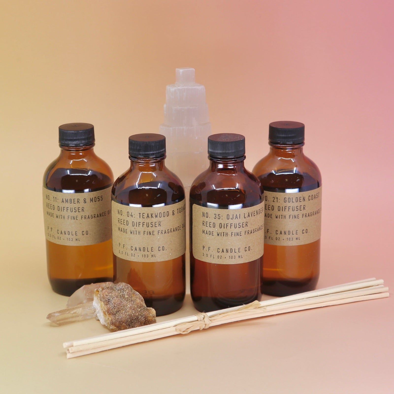 The P.F. Candle Co. Reed Diffusers in front of a selenite tower on a pink and yellow background.