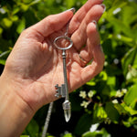 Someone holding the Raw Clear Quartz Crystal Vintage Key Necklace in Silver in front of greenery.
