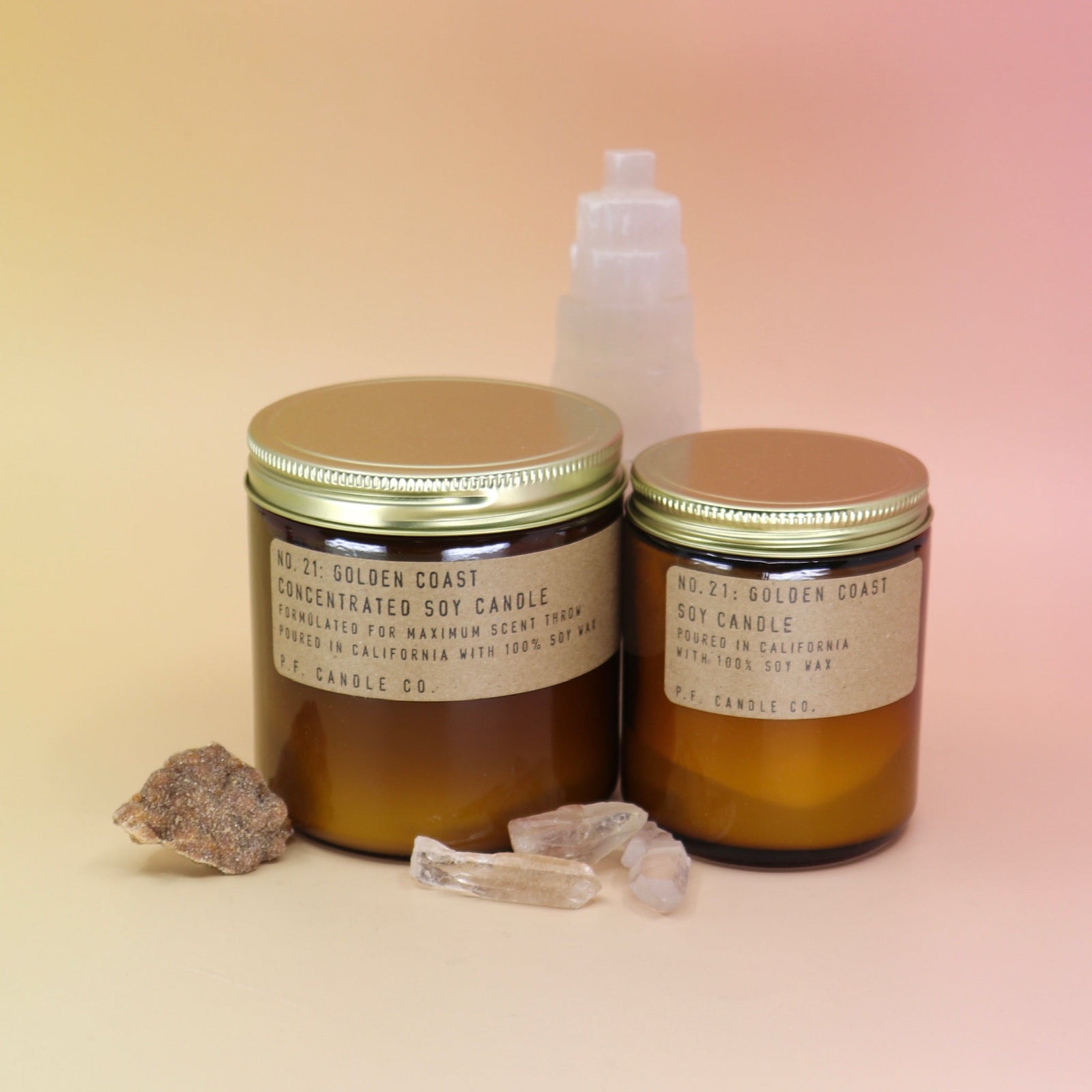 The Golden Coast - 12.5 oz Large Concentrated Soy Wax Candle and regular sized candle in front of a selenite tower all on a pink and yellow background.