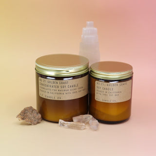 The Golden Coast - 12.5 oz Large Concentrated Soy Wax Candle and regular sized candle in front of a selenite tower all on a pink and yellow background.