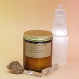 The Golden Coast - 7.2 oz Soy Wax Candle in front of a selenite tower surrounded by other crystals all on a pink and yellow background.