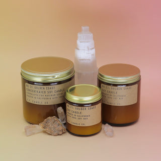 The Golden Coast - 12.5 oz Large Concentrated Soy Wax Candle, travel sized candle, and regular sized candle in front of a selenite tower all on a pink and yellow background.