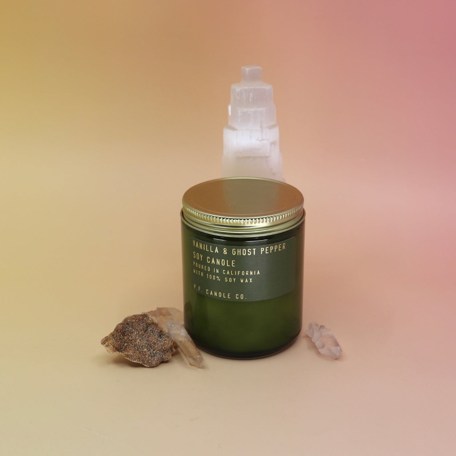 The P.F. Candle Co. - Vanilla & Ghost Pepper Candle in front of a selenite tower on a pink and yellow background.