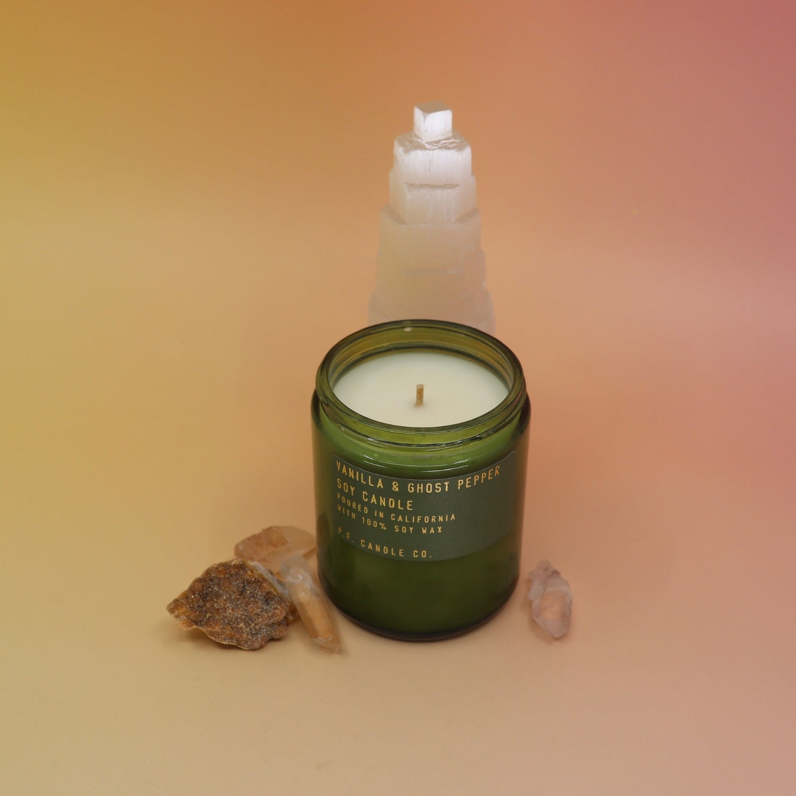 The P.F. Candle Co. - Vanilla & Ghost Pepper Candle in front of a selenite tower on a pink and yellow background.