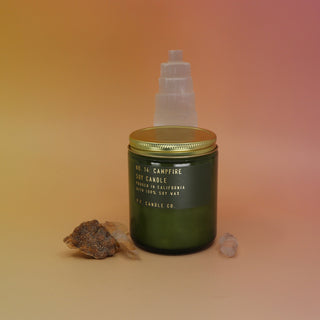 The P.F. Candle Co. Campfire 7.2 oz Standard Candle in front of a selenite tower on a pink and yellow background.