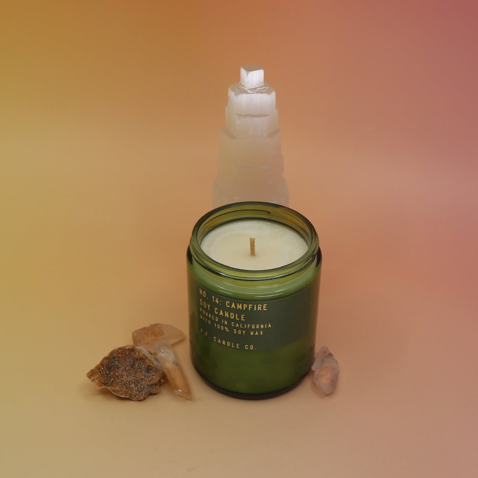 The P.F. Candle Co. Campfire 7.2 oz Standard Candle in front of a selenite tower on a pink and yellow background.