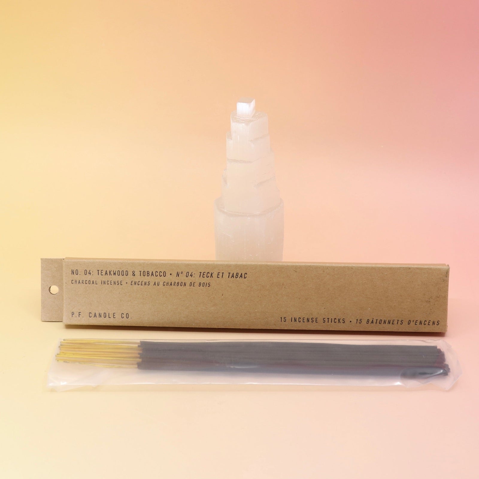 The P.F. Candle Co. Teakwood & Tobacco Incense in front of a selenite tower all on a pink and yellow background.