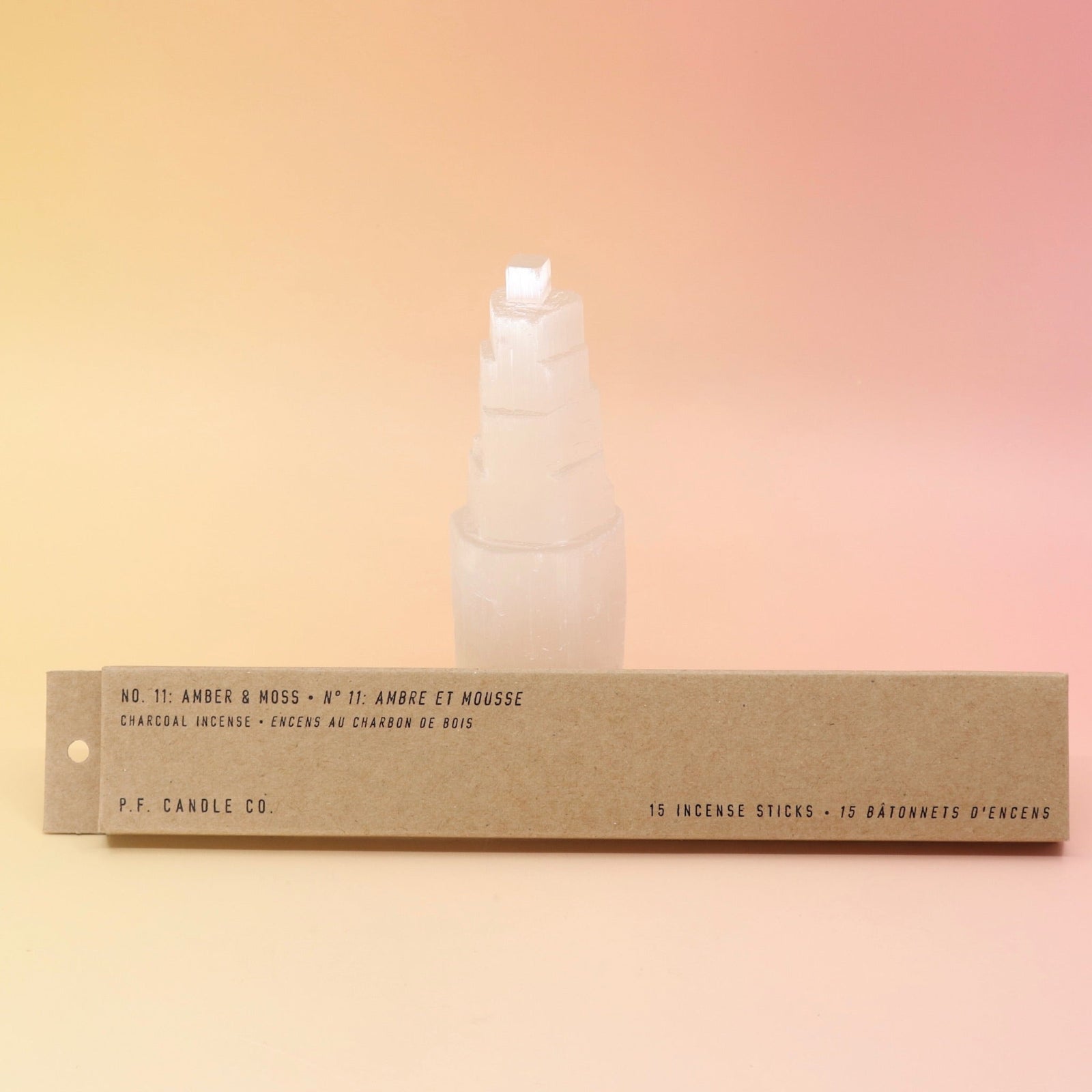 The Amber & Moss Incense - Pack of 15 from P.F. Candle Co. in front of a selenite tower on a pink and yellow background.