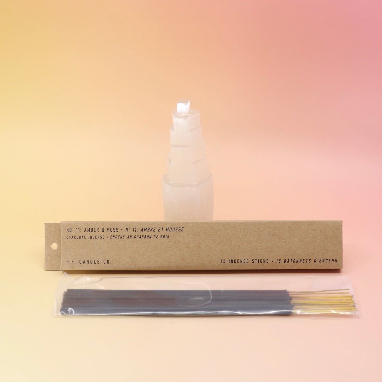 The Amber & Moss Incense - Pack of 15 from P.F. Candle Co. in front of a selenite tower on a pink and yellow background.