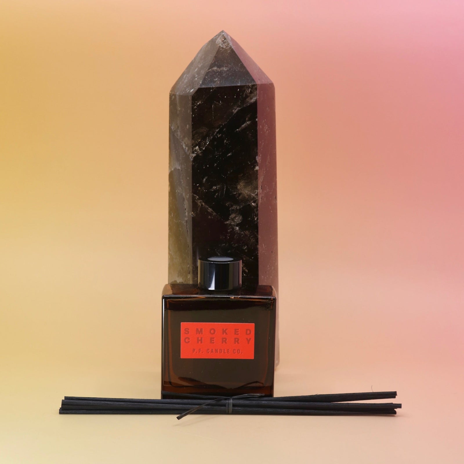 The Smoked Cherry – HI-FI Reed Diffuser in front of a crystal tower all on a pink and yellow background.