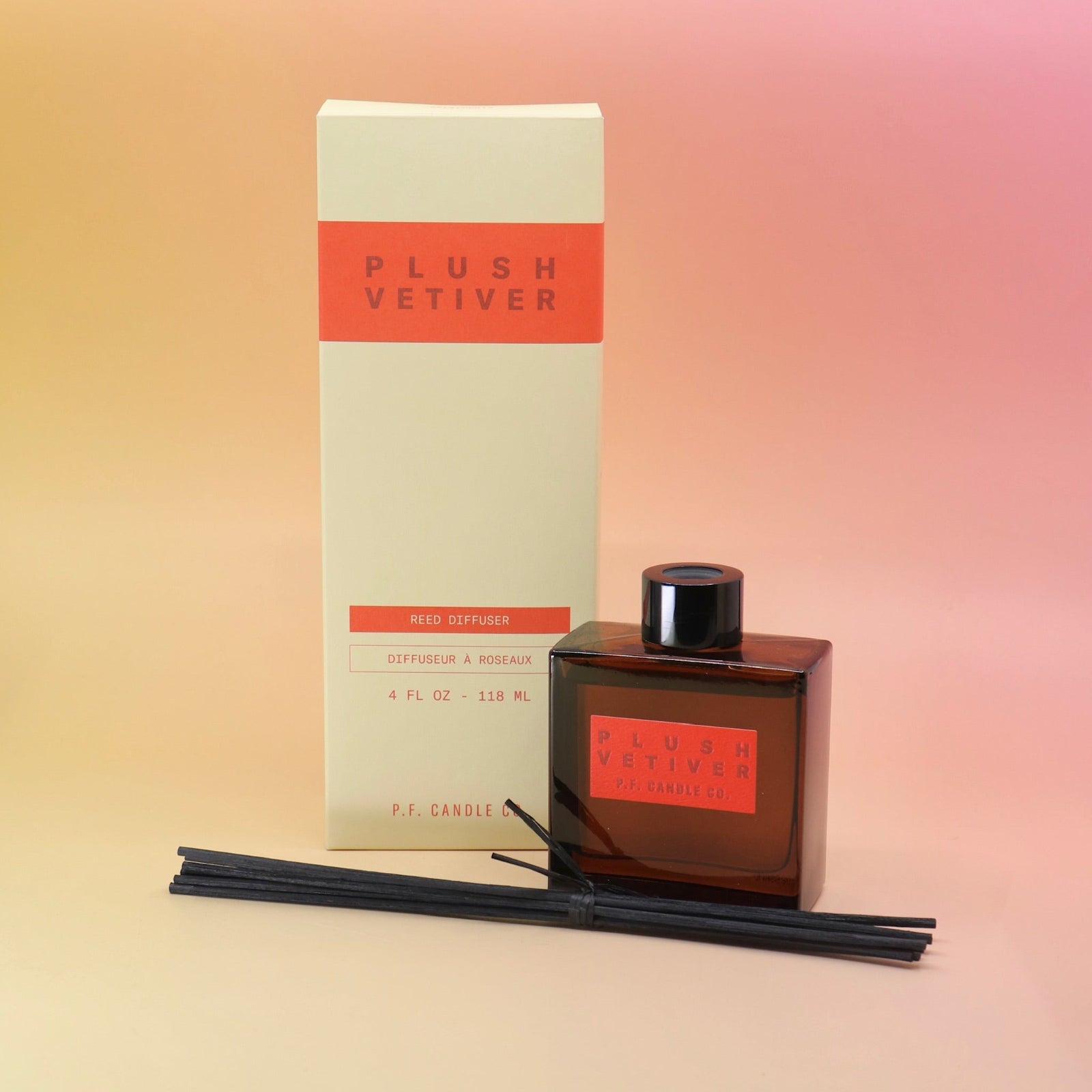 The Plush Vetiver - HI-FI Reed Diffuser bottle next to its to packaging with the reed diffusers in front all on a pink and yellow background.